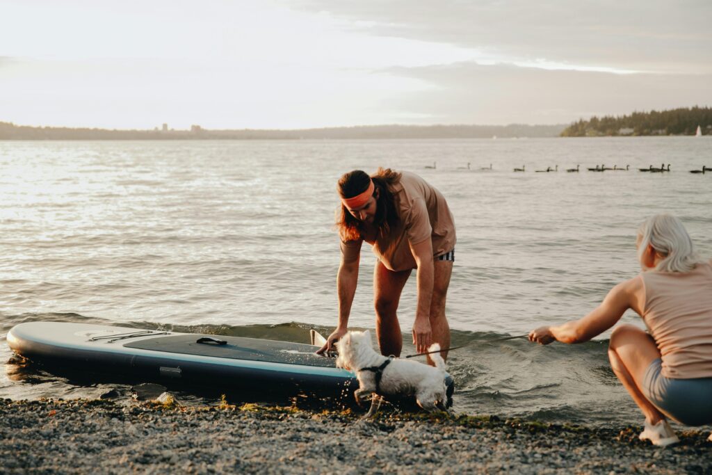 A couple with their dog on a beach setting for a paddleboarding adventure, embodying summer fun.